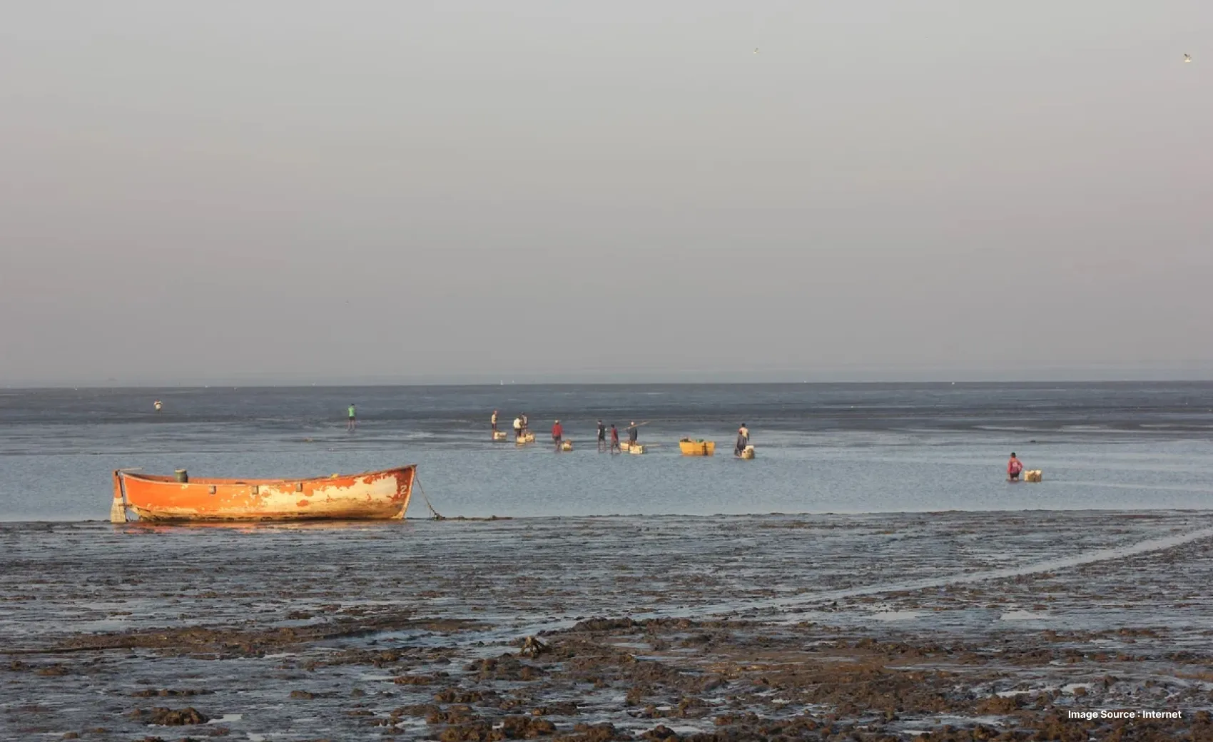 a coastal shore with a rusty looking boat parked as people enjoy further down in the sea