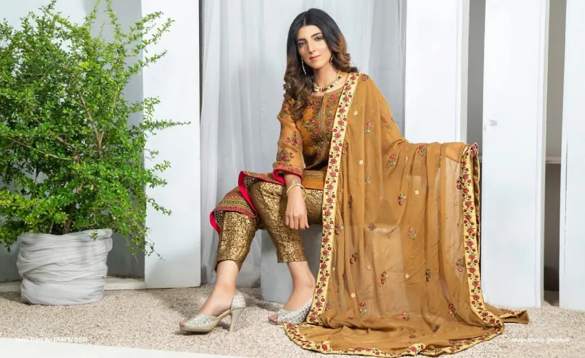 A picture of a woman wearing a dark peach-toned kurta showing off her duppata scarf.