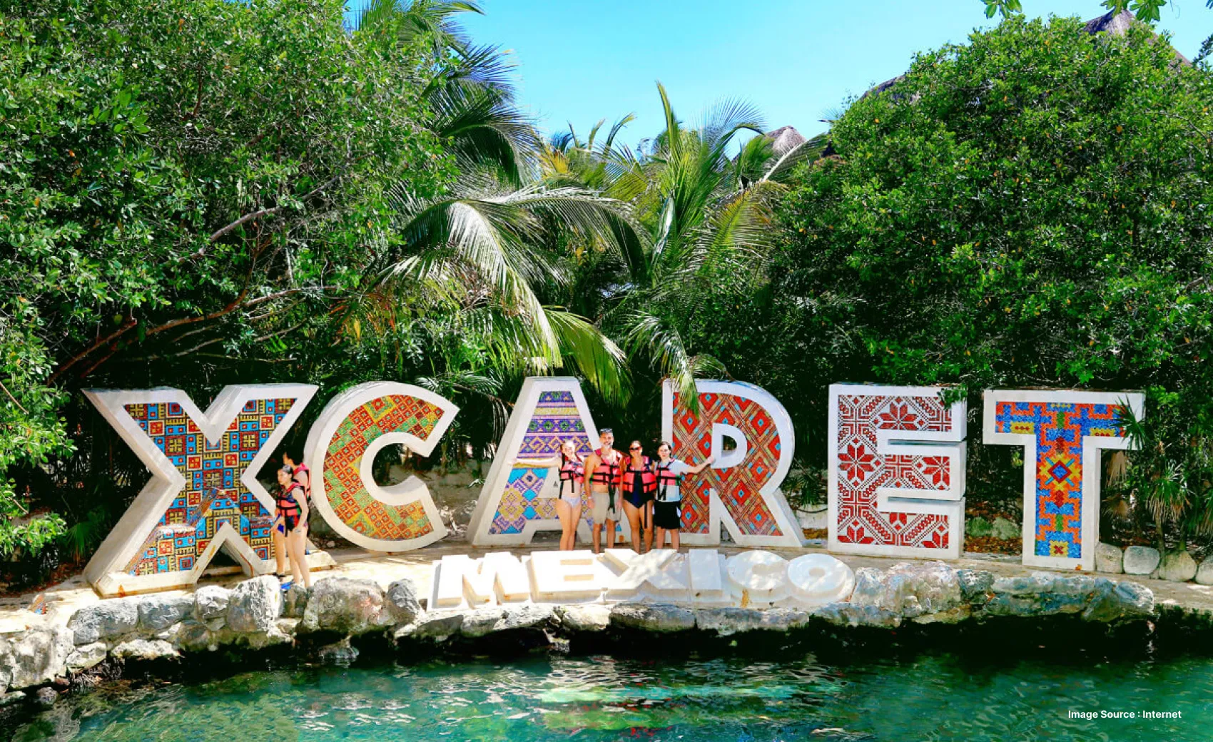 tourists in safety vests posing in front of the colorful xcaret mexico signboard