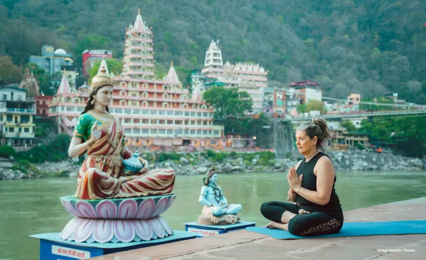 a white woman practicing yoga in rishikesh besides a hindu goddess and god's idol