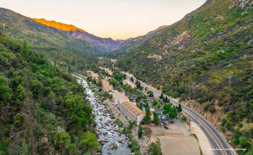 a small motel building in midst of a serene mountain landscape at sunset, right besides a river