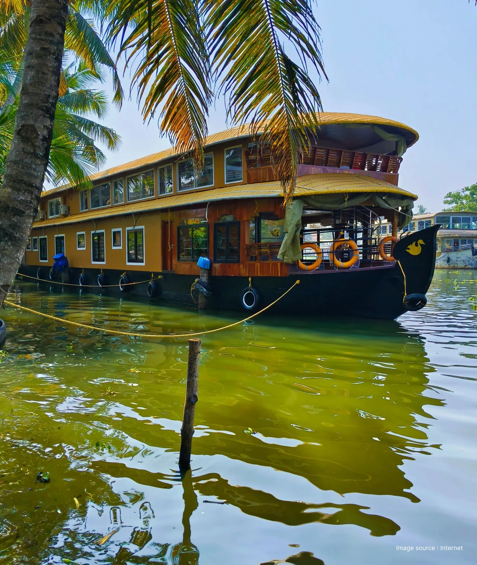 a traditional two storeyed houseboat parked by a palm tree on kerala backwaters