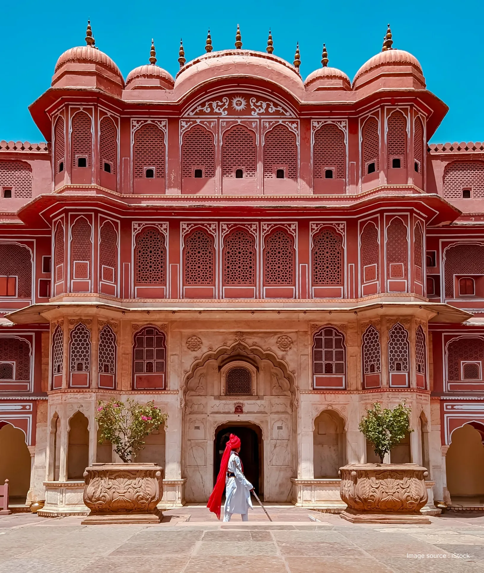 a local in a red turban walks past the entrance of a beautifully painted wing in the city palace