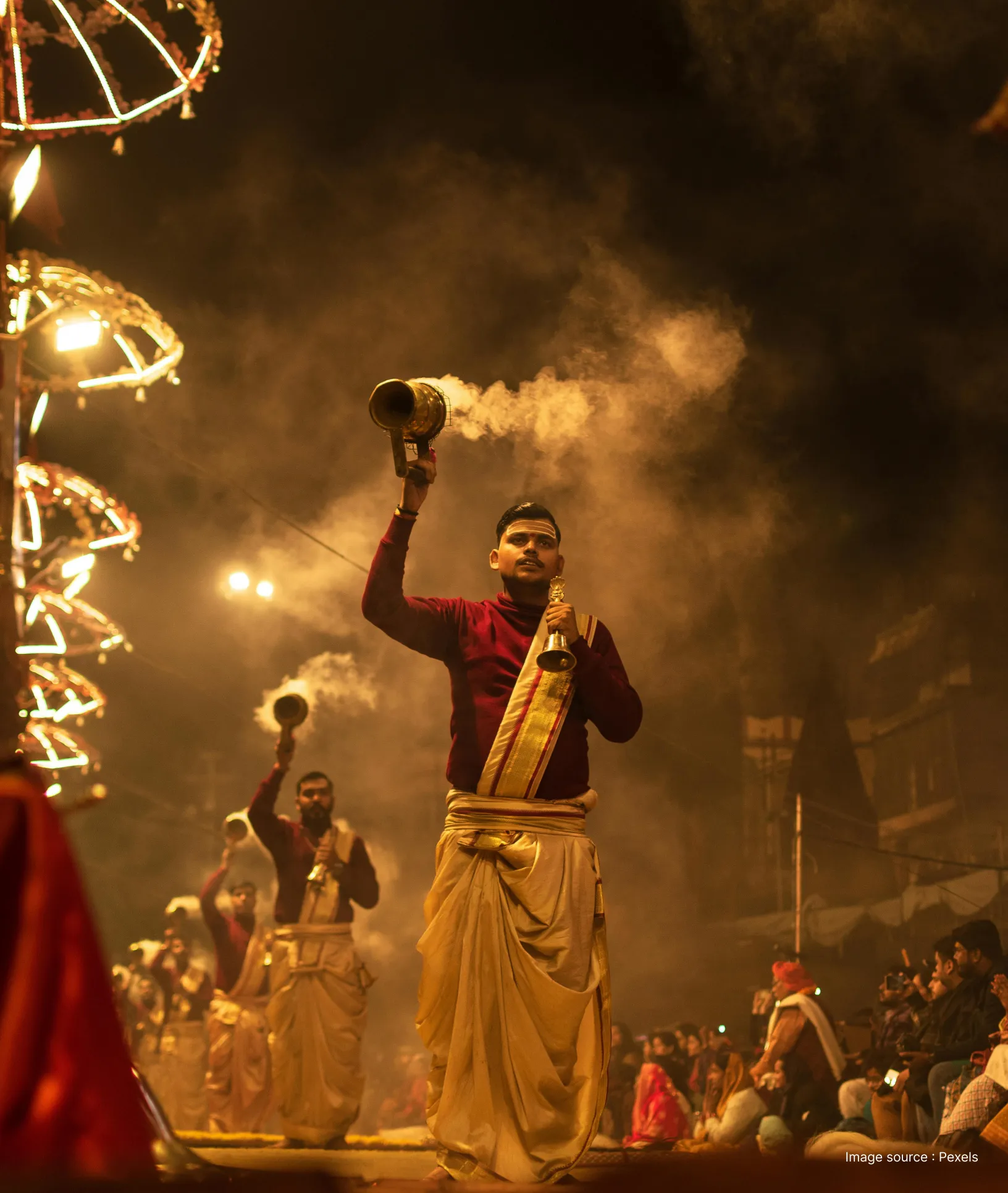 front view of a priest performing the ganga aarti with a holy bell and prayer lamp at dusk
