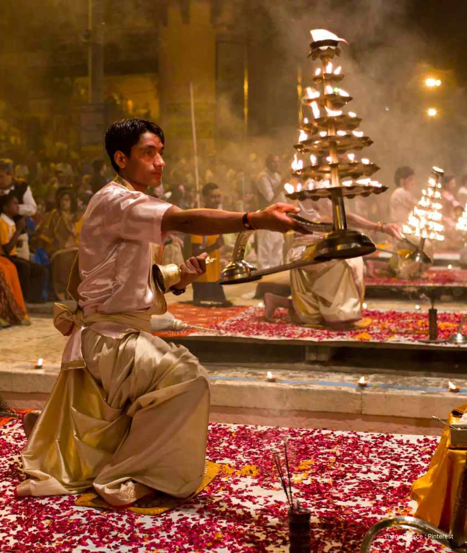 front view of a priest performing the ganga aarti with a large prayer lamp at dusk