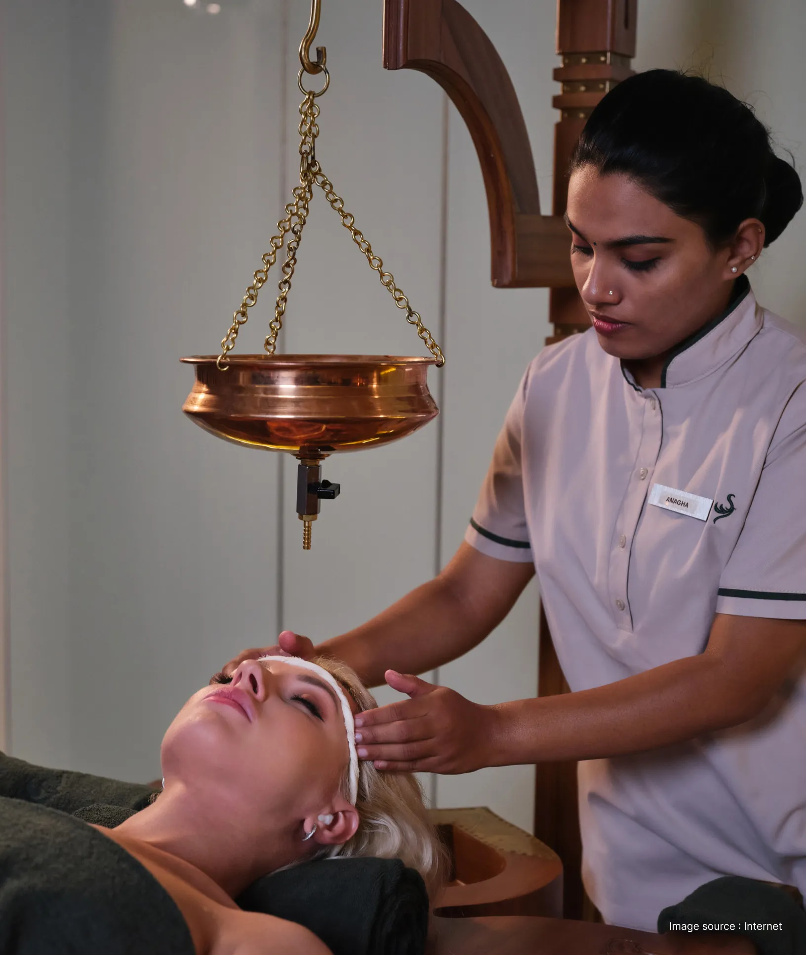 an ayurvedic therapy in progress as a uniformed woman massages oil on clients forehead