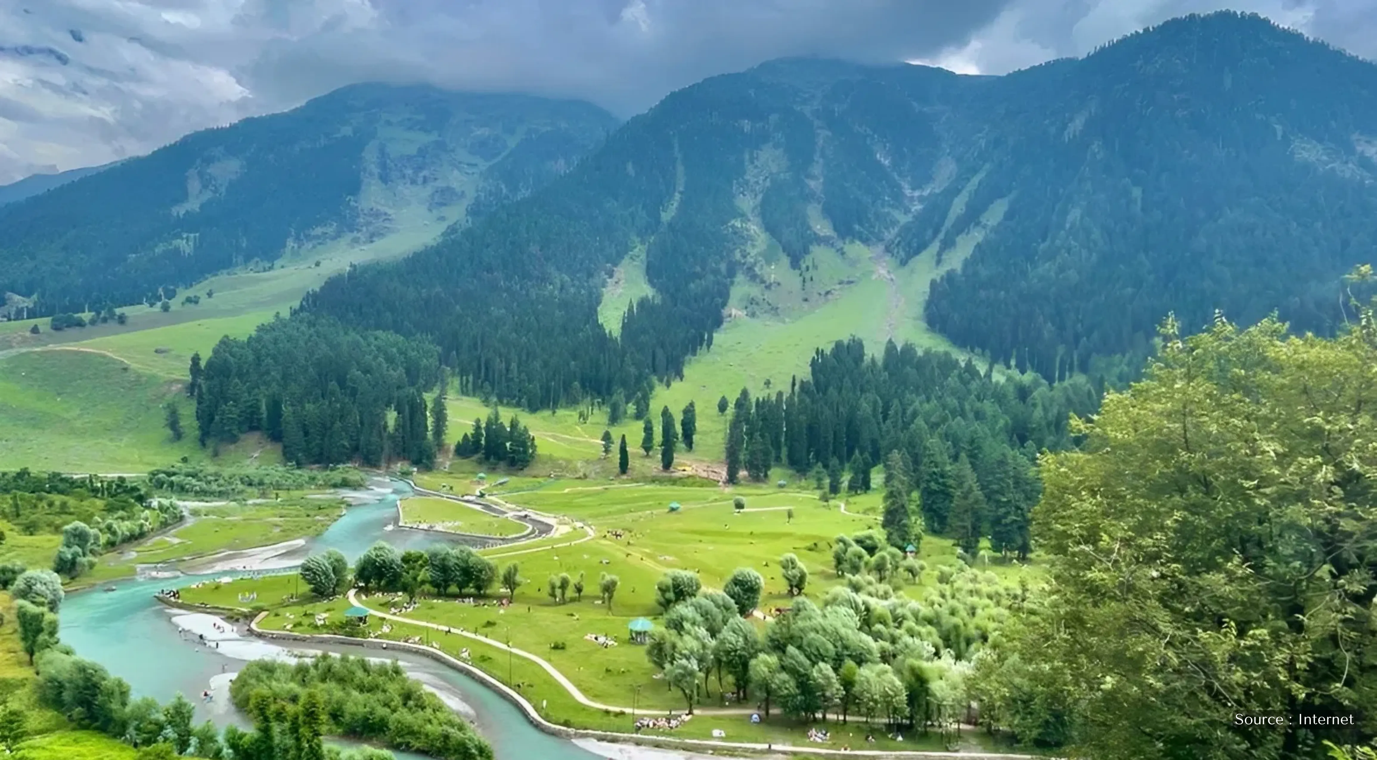 Panoramic view of the lush green Pahalgam Valley in Kashmir, featuring a winding road through pine forests under a clear blue sky.