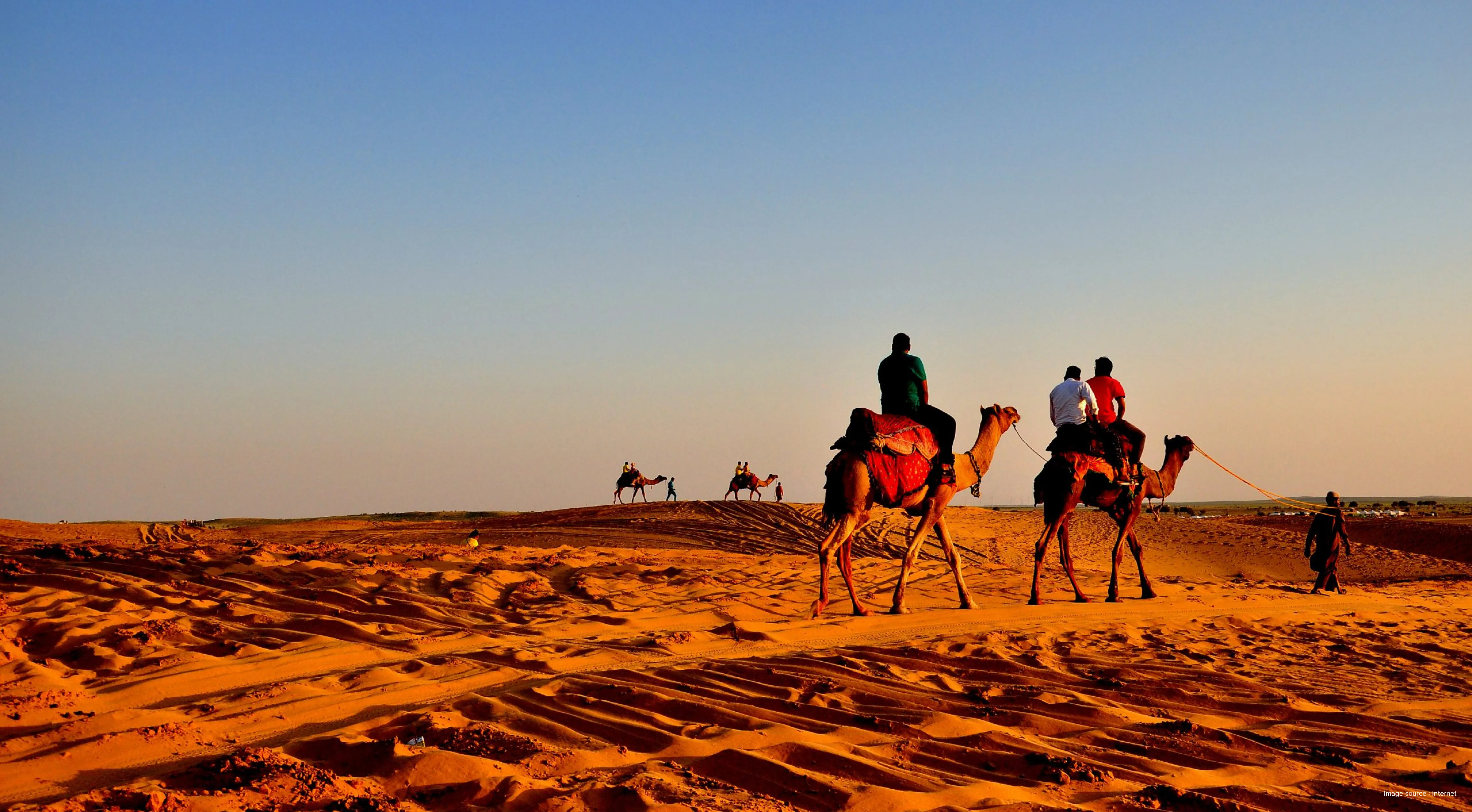 A sunset view of rajasthan desert with 3 camel riders going with their camels