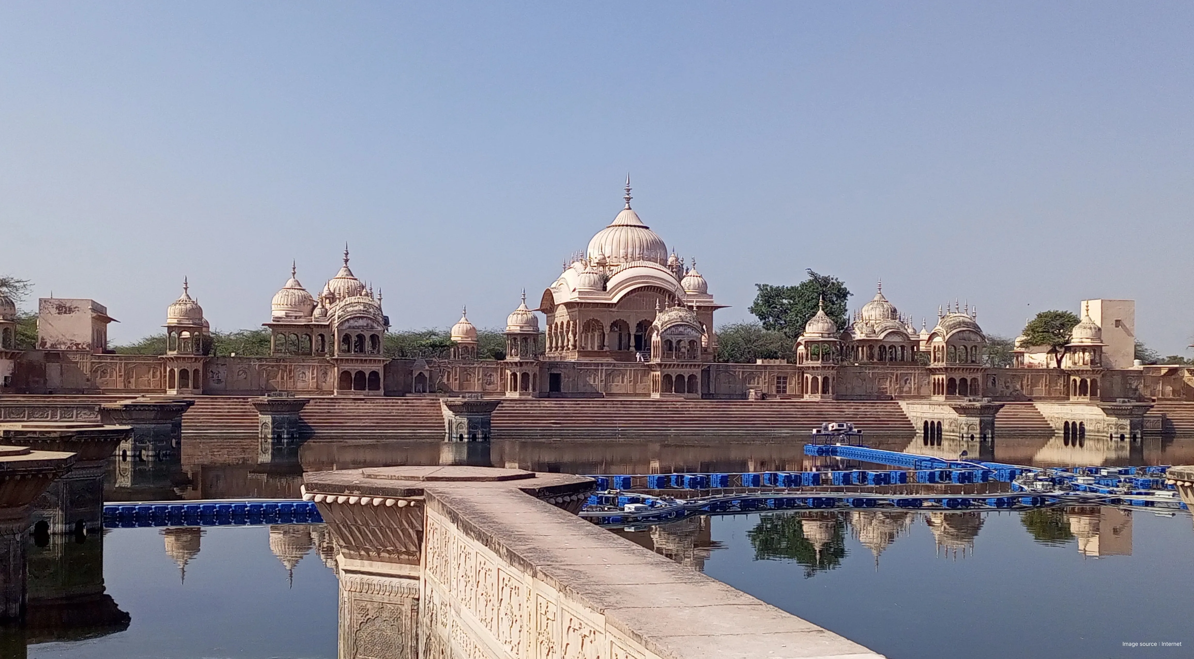 Wide panoramic view of the historic Kusum Sarovar lake showing the grand architectural reflection in the water.