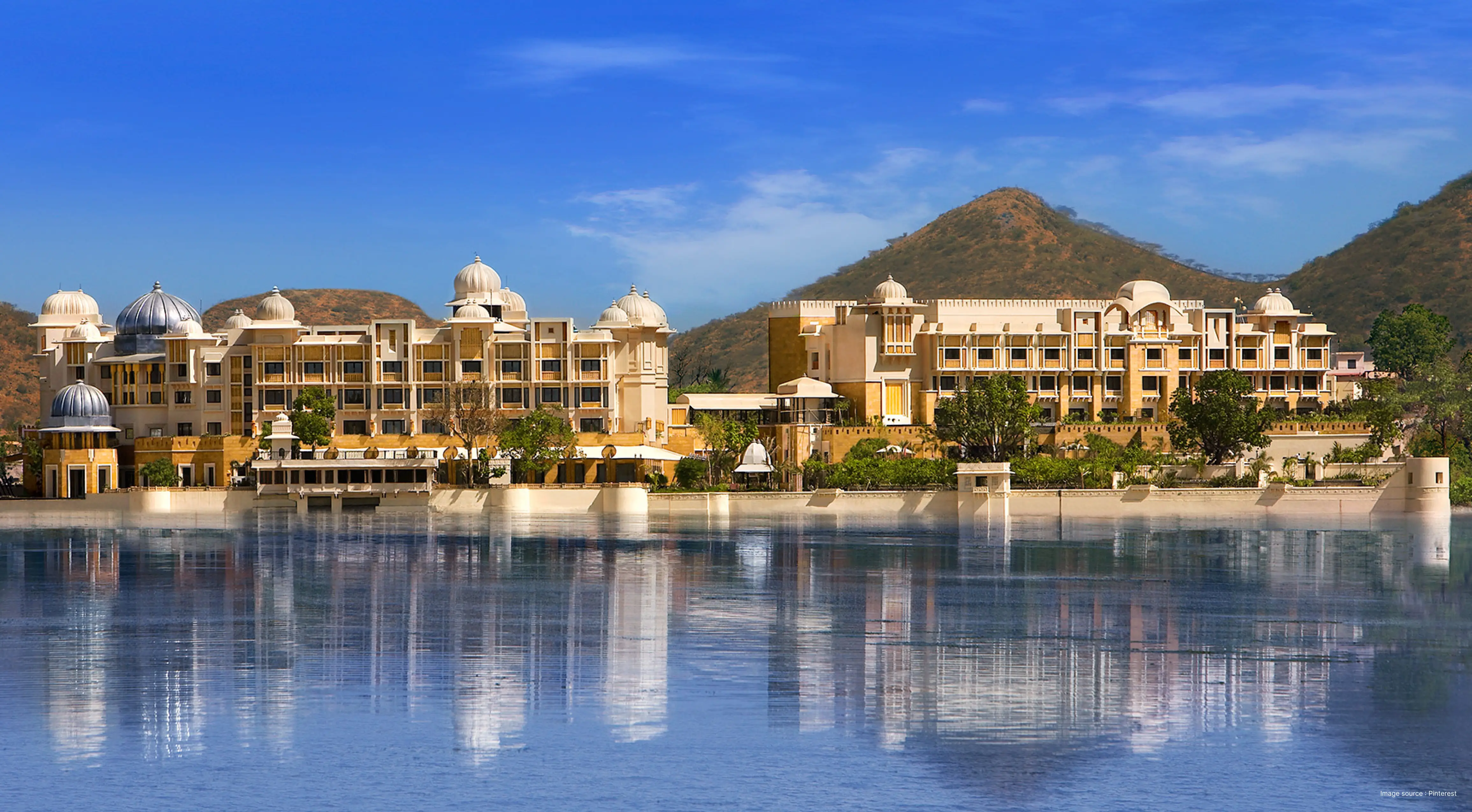 view of the magnificent lakeside leela palace in udaipur with green aravallis in the backdrop and a clear sky