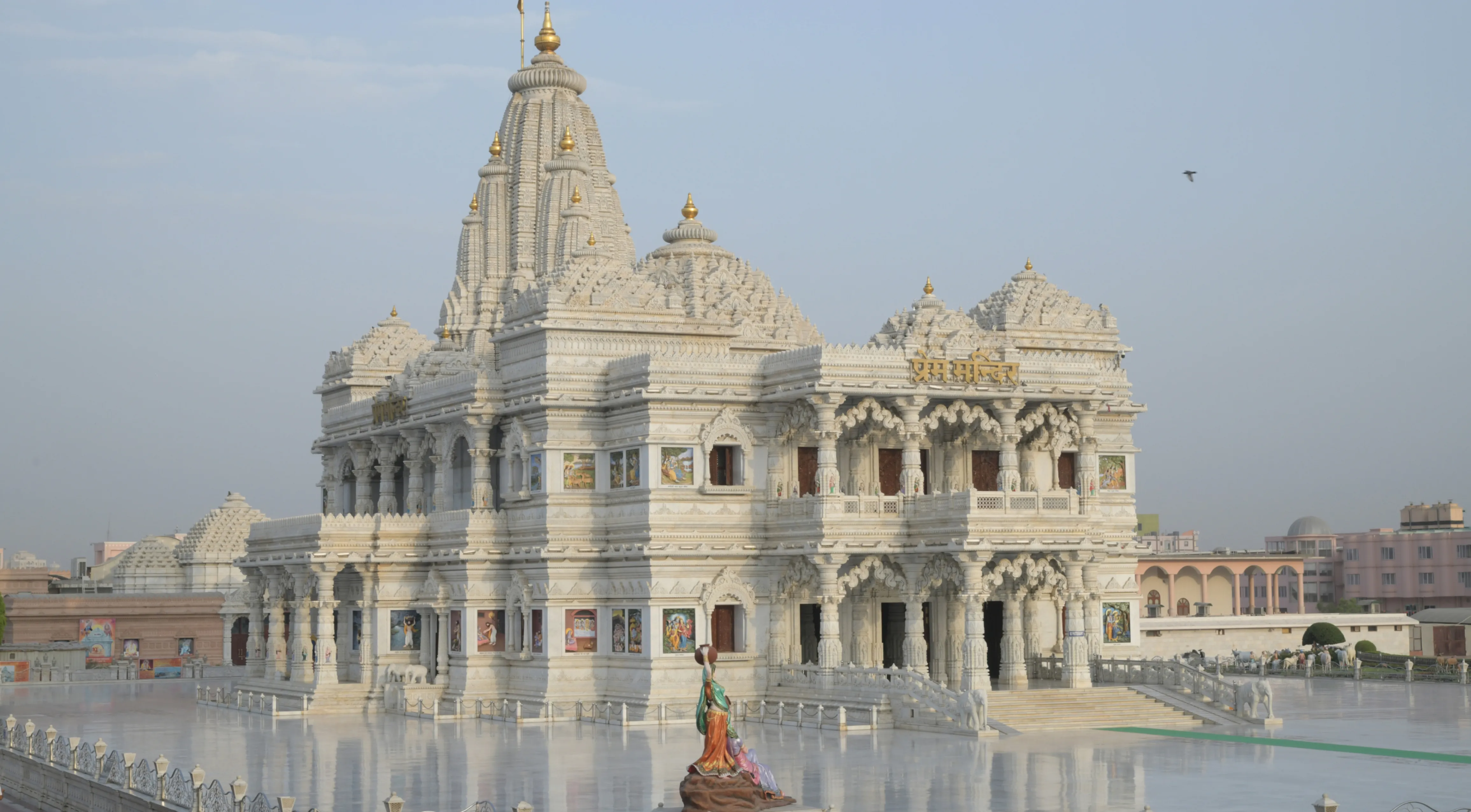 The white marble architecture of Prem Mandir in Vrindavan, featuring intricate carvings, multiple levels, and a central shikhara under a clear sky.