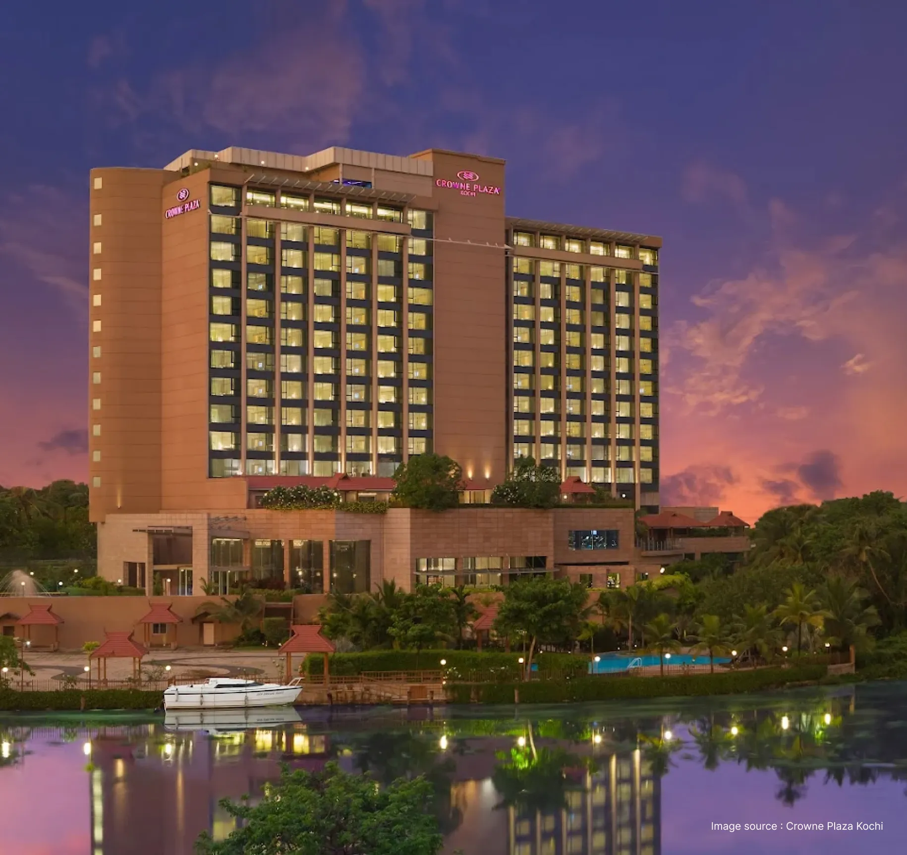sunset view of the crowne plaza in kochi with all rooms lit up and the pool area visible