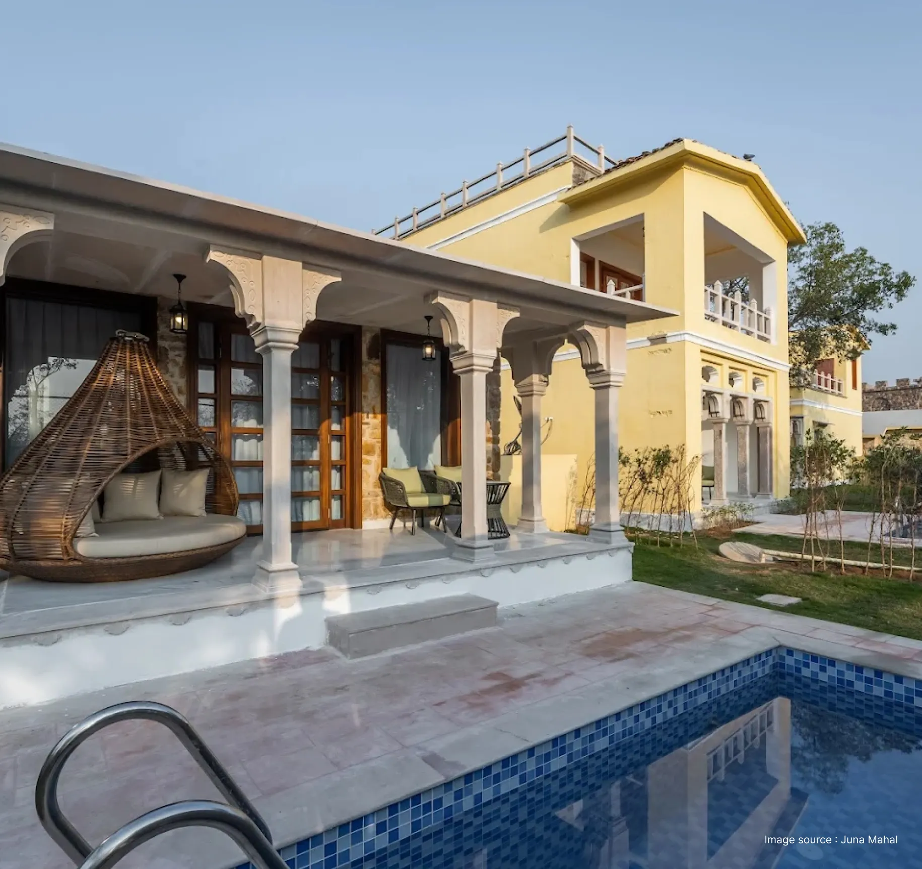 a poolside view of a yellow hotel building with lounge chairs