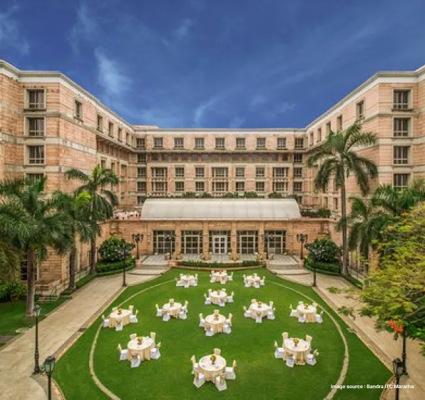 A hotel front yard with 3 buildings surrounding it and banquet seating infront of it