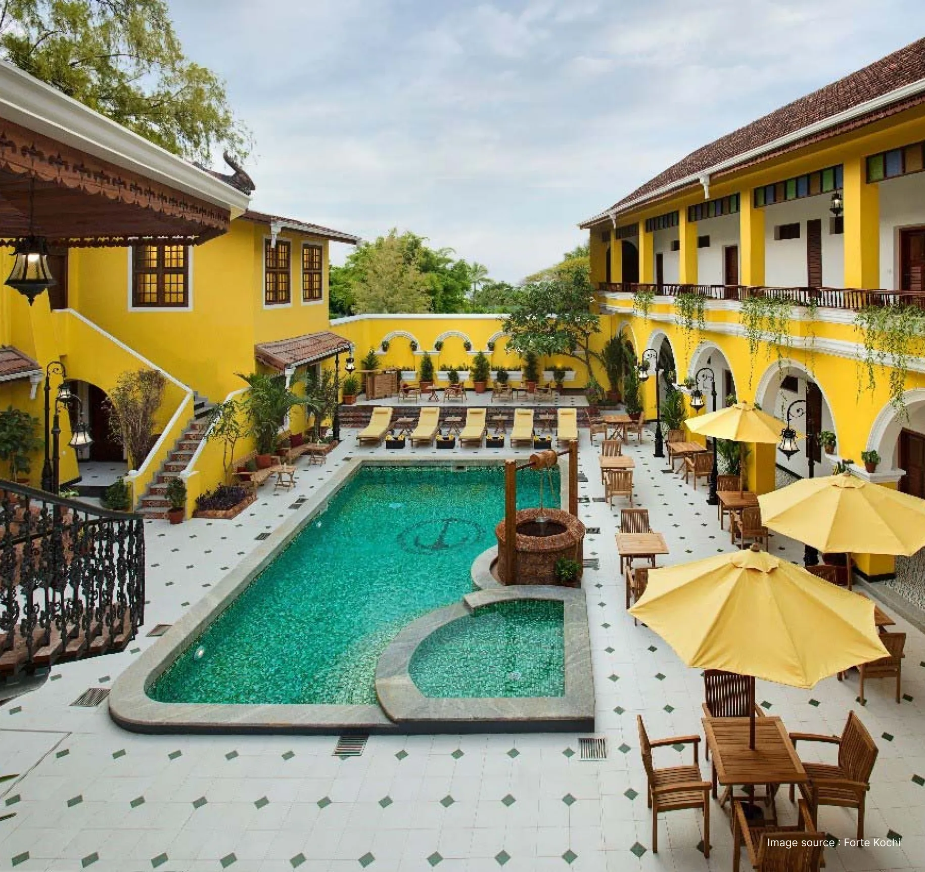 portuguese inspired building of the forte kochi hotel with striking yellow walls and pool area with wooden seating and a wooden well
