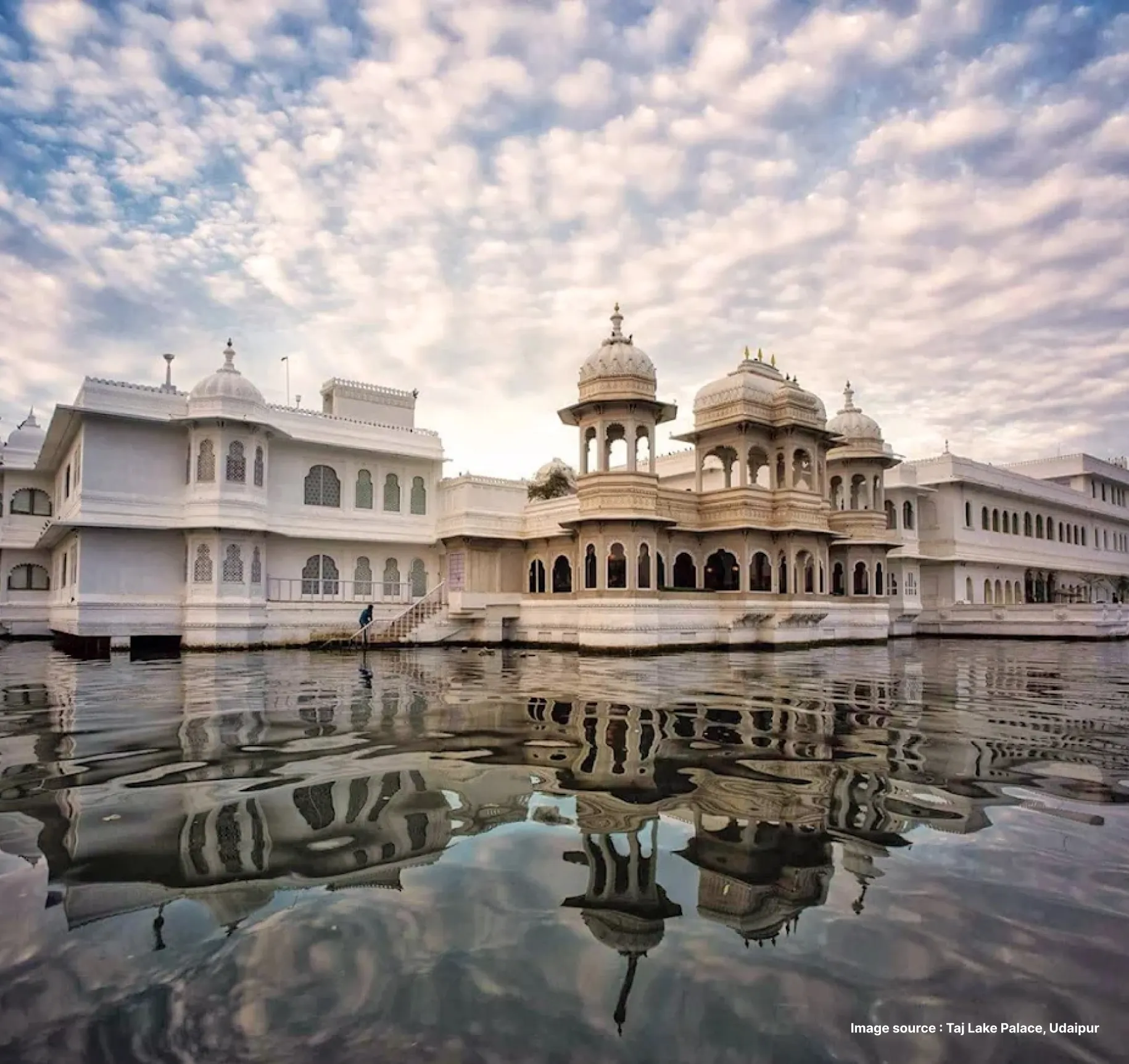 a dramatic view from the lake of the ethereal white building of the taj lake palace on a cloudy day