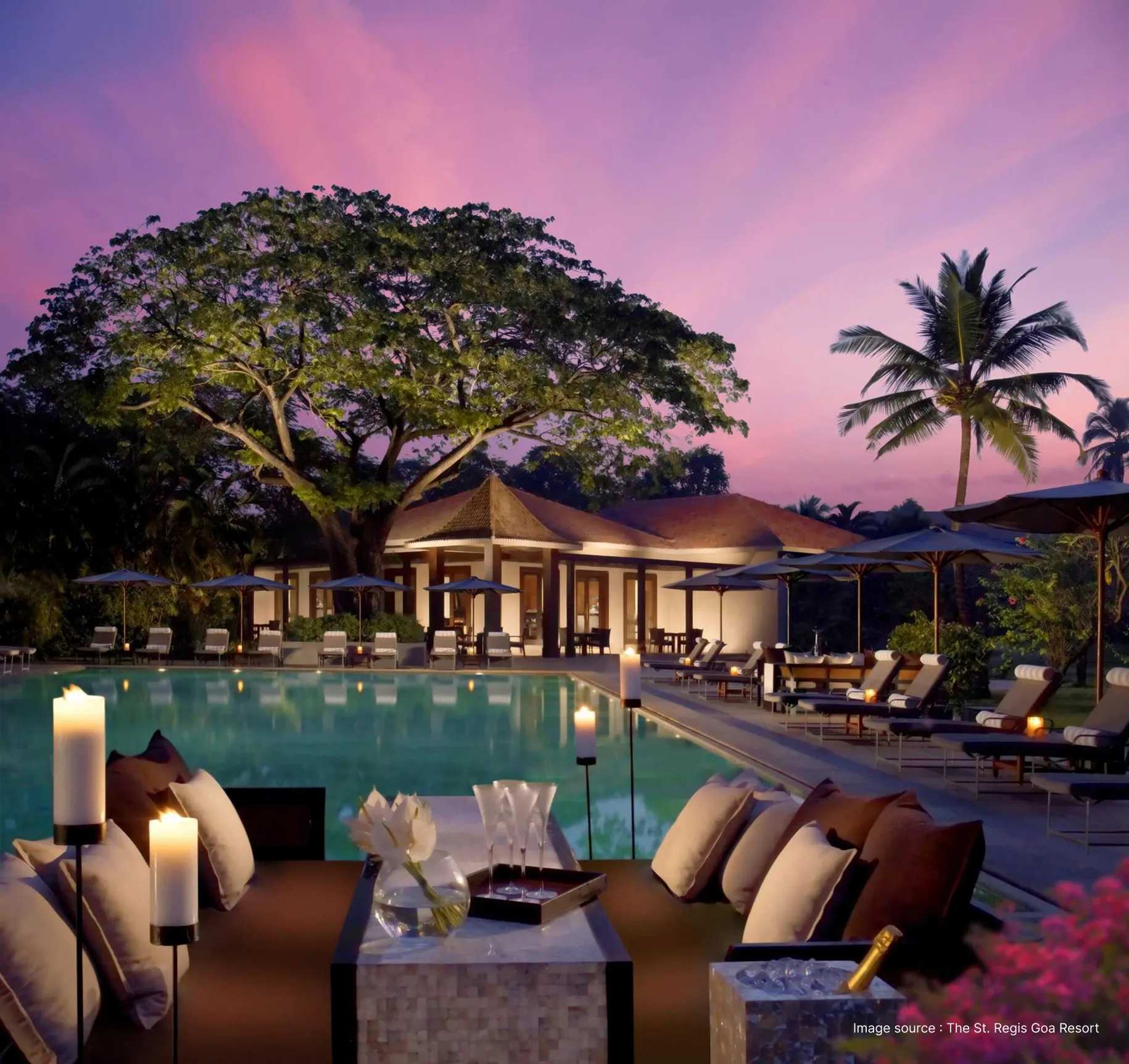 pool area of the st. regis goa at sunset with dining set up and big trees