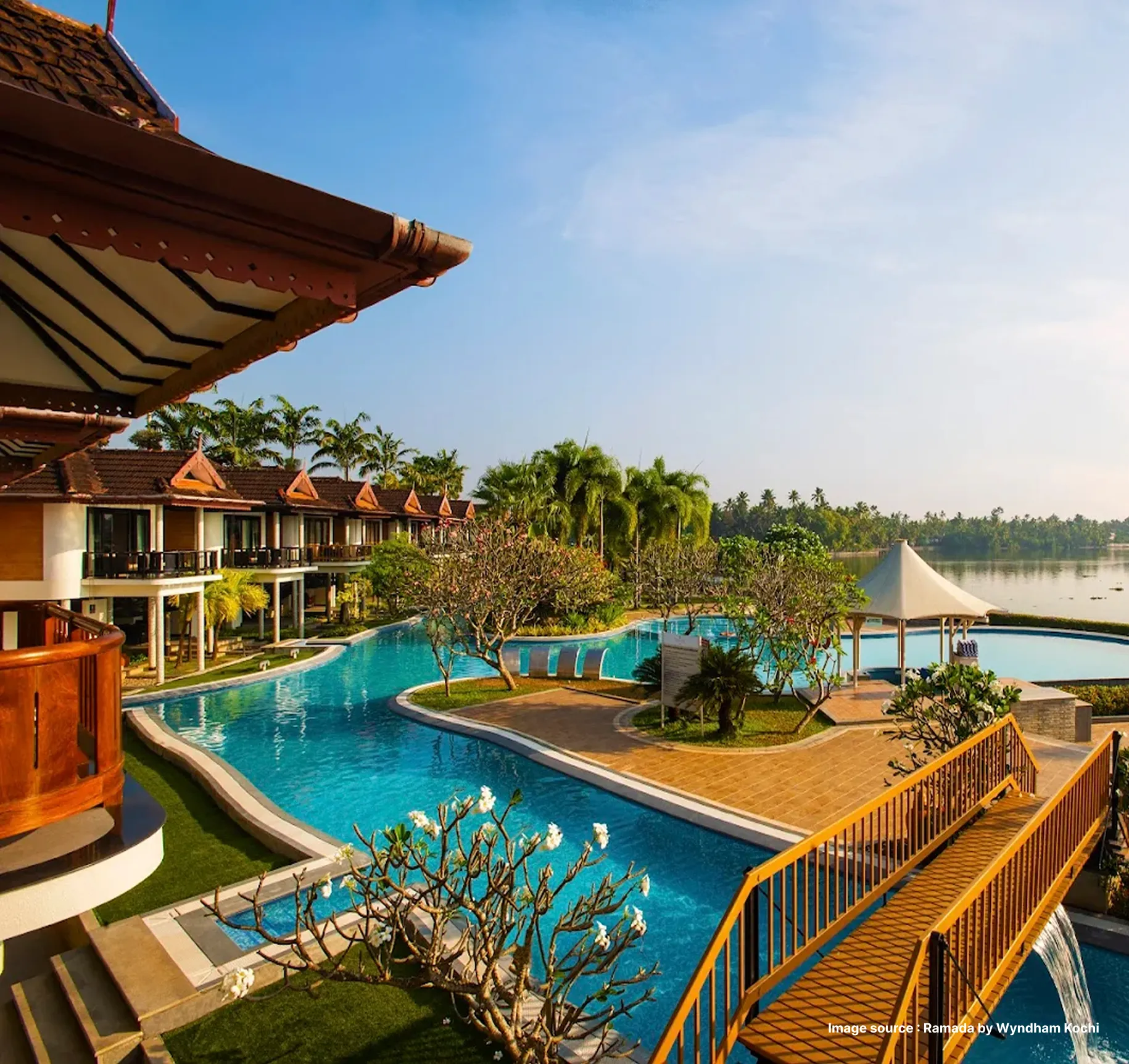 unique poolside view with wooden deck and palm trees in a distance of ramada hotel in kochi
