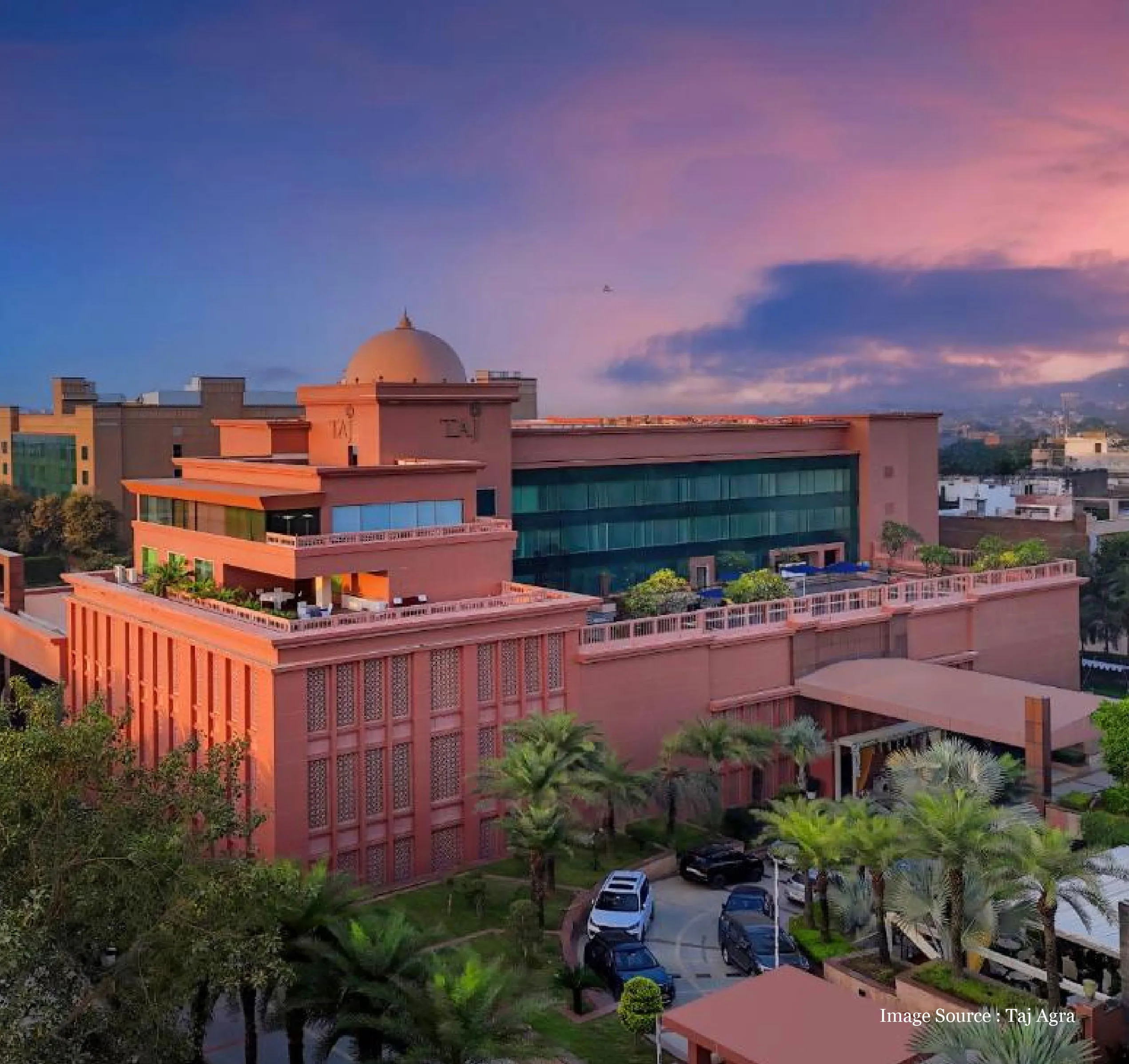 side view of the taj hotel in agra with red dome and lush green trees during a sunset