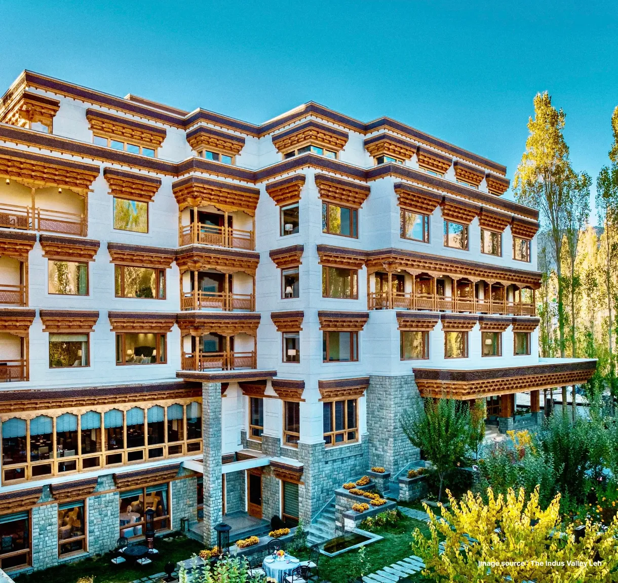 a traditional ladakhi style white building with orange accents surrounded by plants