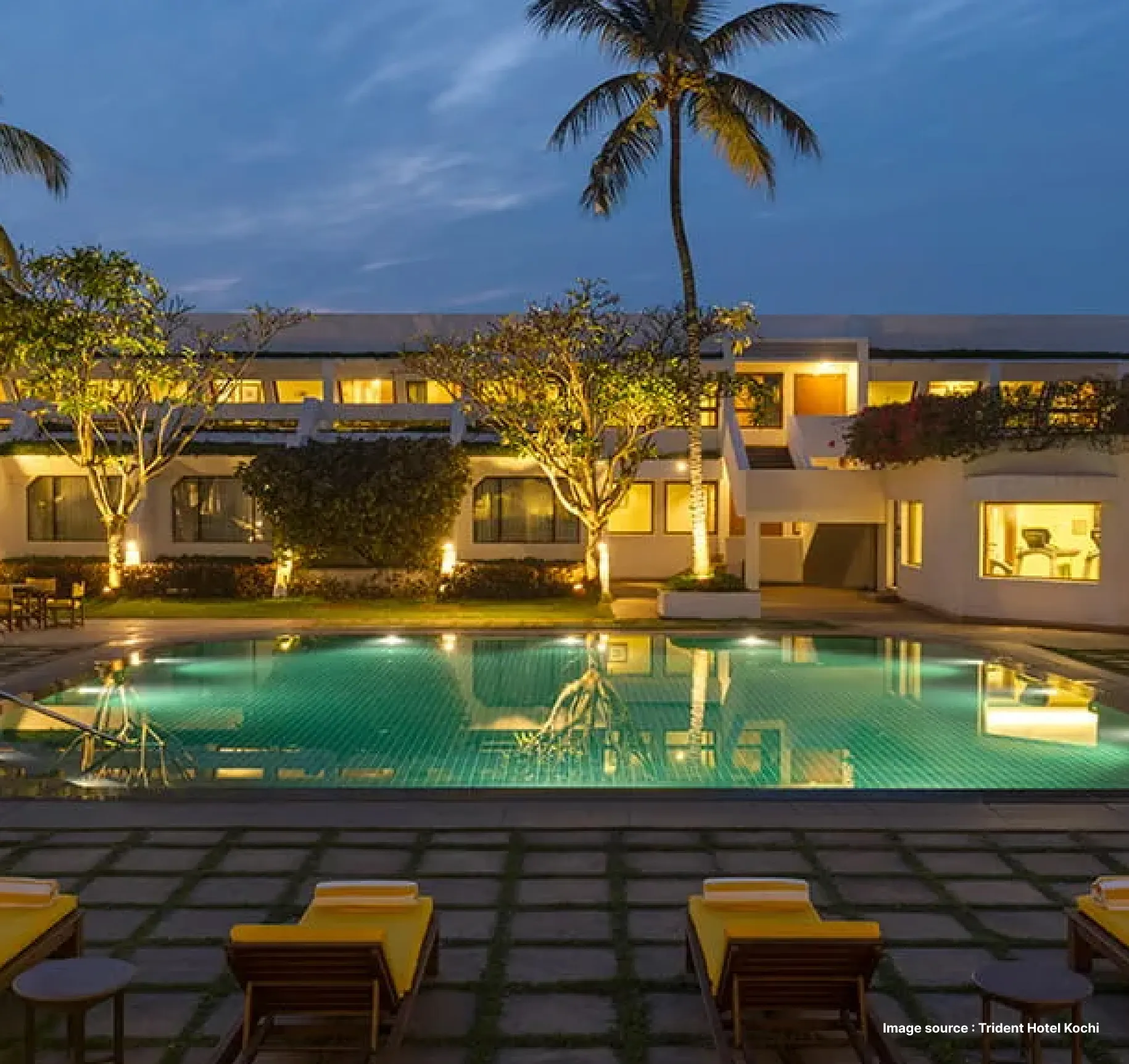 modern pool area view with lounge chairs and palm trees at dusk with the lit up trident hotel corridors