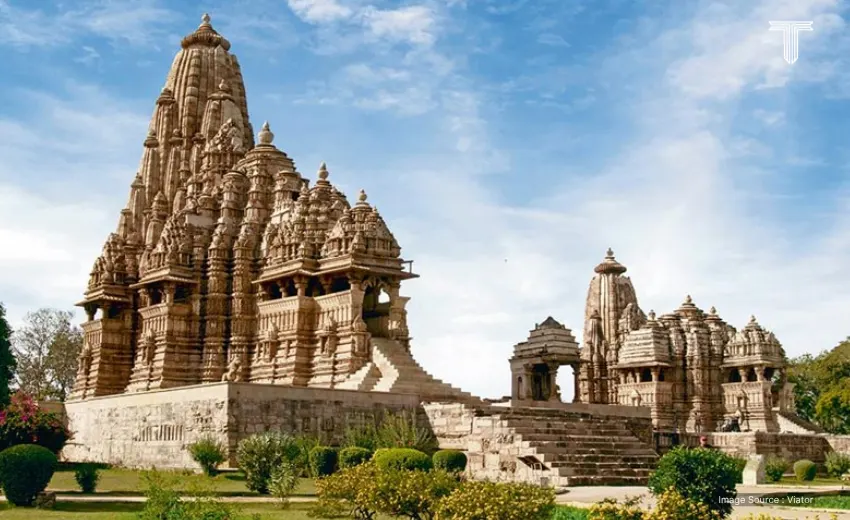 A private luxury travel planning in traditional attire explaining intricate carvings at Khajuraho Temple, with guests enjoying champagne under shaded umbrellas.
