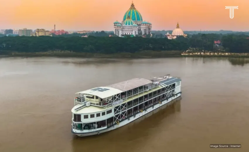 An intimate scene on the private boat's upper deck in ganga river cruise. Guests relax on plush loungers, sipping chai, as a guide points towards the vibrant and intricate rituals of the Ganga Aarti ceremony taking place on the nearby ghats. 
