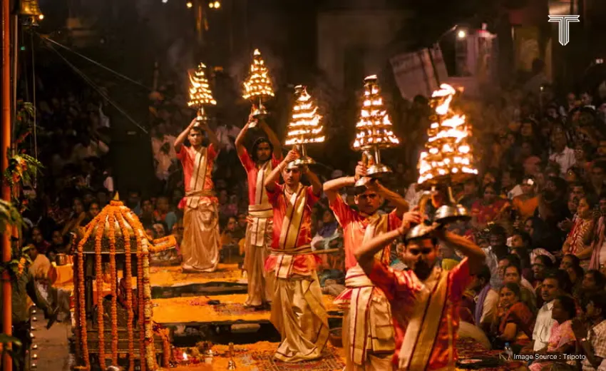 A table set on a palace terrace at dusk, featuring gold-rimmed thalis filled with regional delicacies like malaiyo and tamatar chaat, overlooking illuminated ghats in Varanasi tour packages.
